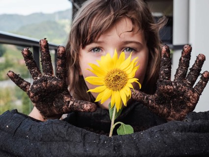 A young girl showcases her muddy hands while clutching a bright sunflower, symbolizing the