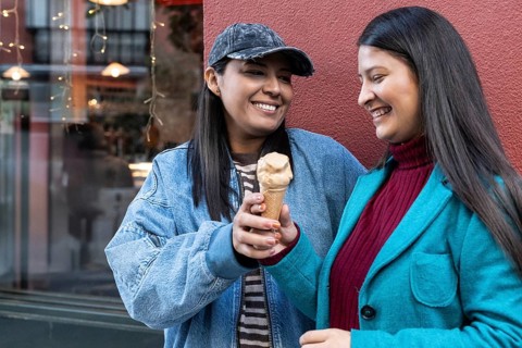 A joyful Latin lesbian couple shares an ice cream cone in a vibrant urban setting, showcasing