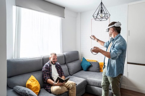 One man uses a VR headset, fully immersed in a virtual world, while his partner relaxes on the