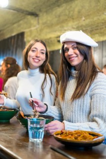 Vertical photo of two stylish women eating ramen soup in a restaurant