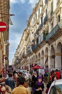 Busy street with many people and shops, surrounded by historic buildings with balconies under a