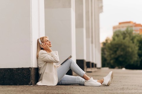 A businesswoman sits relaxed on the ground, listening to music through headphones. She leans back