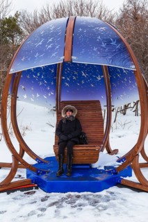 Woman sitting and relaxing in cocoon rocking chair made of curved wood and blue tinted plexiglass