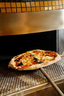 A freshly baked pizza with basil and cheese topping out of an industrial pizza oven