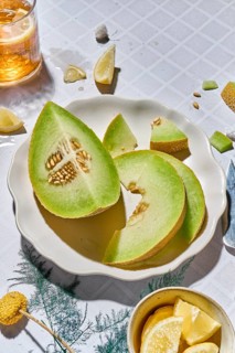 Top view of fresh green melon slices and yellow lemon wedges on a white tiled ceramic plate. The