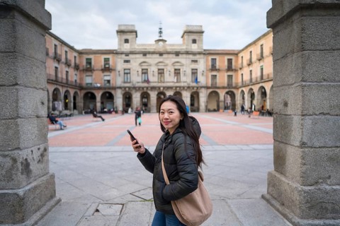 An Asian female tourist explores the iconic medieval and historic streets of Avila, Spain. She