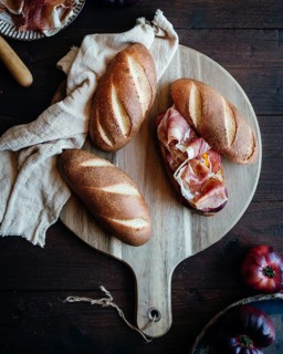 A rustic wooden board displays olive oil bread topped with savory Serrano ham and tomatoes,