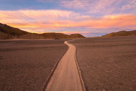 A tranquil desert scene features a winding path under a stunning sunset in the argentine Puna. The