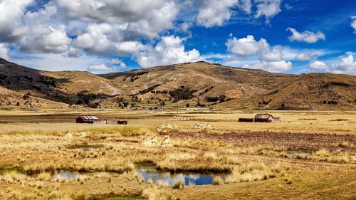Scattered huts and swampy areas under a mountainous and cloudy landscape, The villages and