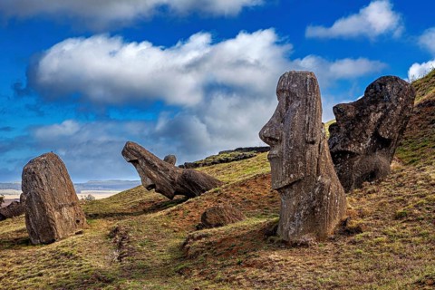 Stone figures on a grassy hill under blue sky with clouds, The Moai Statues on Easter Island in the