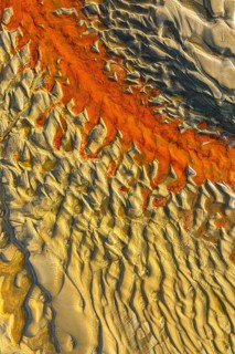 An aerial view reveals intricate sand patterns with vibrant orange and beige tones. The natural