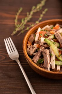 Meat salad with beef and vegetables in wooden bowl on brown wooden background and linen textile.