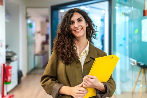 Portrait of a businesswoman holding a yellow folder, smiling in a modern office environment