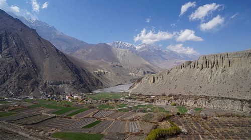 View of a green valley surrounded by high mountains under a slightly cloudy sky, trekking at