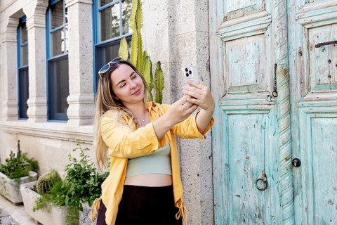 A female tourist joyfully takes a selfie on a vibrant street. Her yellow jacket contrasts with the