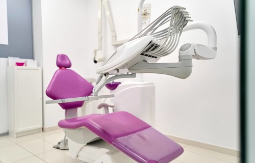 A contemporary dental clinic room features a sleek purple dental chair, advanced equipment, and a