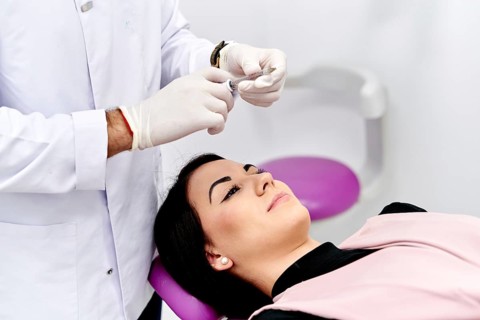 A patient receives a facial cosmetic treatment in a medical clinic. The doctor prepares for the