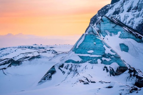 Vibrant sunset light washes over jagged blue ice formations at Katla Glacier in Iceland. The vivid