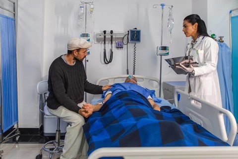A doctor consults with a patient's family member at the bedside in a hospital room. The patient is