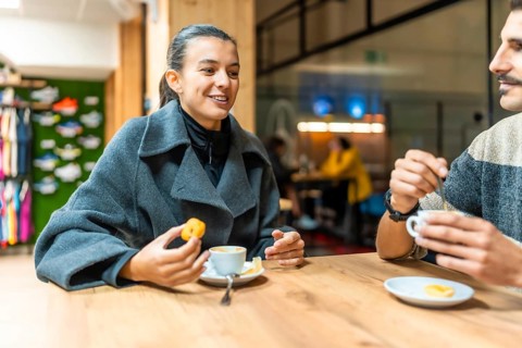 Young man and woman sitting at a wooden table, enjoying coffee and a snack while having a pleasant