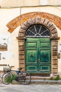 Weathered old arched entrance door, in front of it a parked bicycle, historic city centre, Lucca,