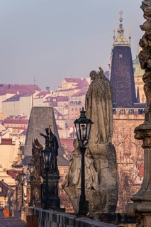 An evocative view of statues on Charles Bridge overlooking the historic rooftops of Prague during a