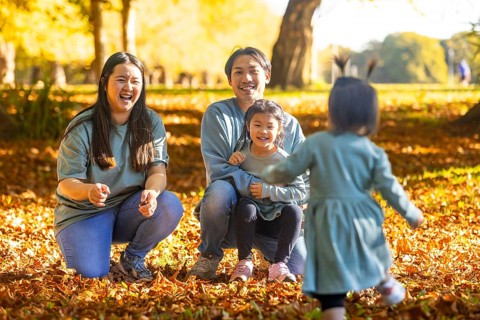 Joyful Asian family enjoying a playful afternoon in a scenic autumn park, surrounded by fallen
