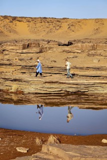Two people walking over stone slabs in a vast desert landscape, Tuareg fetching water in the Sahara