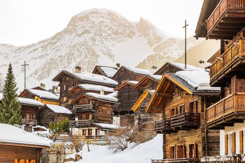 Snow-covered old farmhouses, large wooden cross, historic town center, in the back the snow-capped