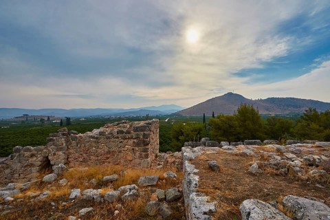 Ancient ruin landscape with a view of a mountain range and cloudy sky in the background, Tiryns,