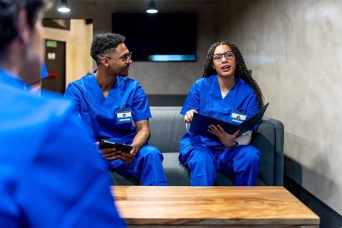Healthcare professionals wearing blue scrubs and identification badges are discussing notes and