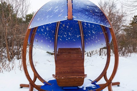 Interactive cocoon rocking chair made of curved wood and backlit blue tinted plexiglass panels