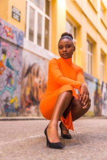Fashionable urban style with a black African girl in an orange dress and black heels on a city