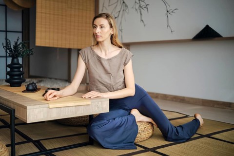Focused woman sits on a mat with her legs crossed at a low table. The room has minimal decor with