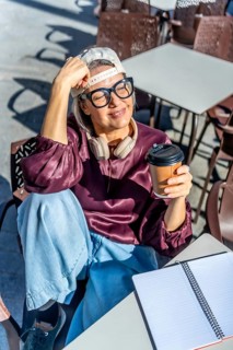 Stylish woman relaxing at an outdoor cafe with eyes closed, savoring hot coffee from a disposable