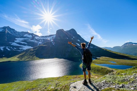 Hiker stretches his arms in the air, in front of mountain landscape with lake Giklingdalsvatnet,
