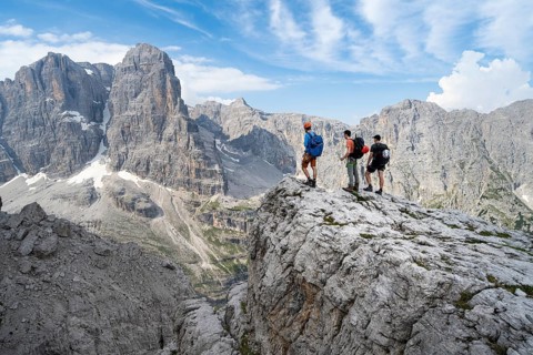 Three mountaineers on a rock in front of a picturesque mountain landscape with rocky peaks, Via
