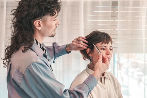 Professional makeup artist using comb and brush while preparing model's face for fashion show,