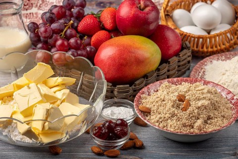 Ingredients for baking cake next to basket with grapes, apples, strawberries and mango