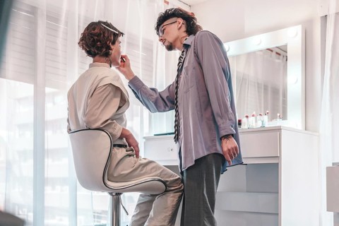 Professional makeup artist carefully applying lipstick on a client sitting in a chair in front of a