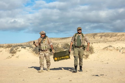 Two soldiers in camouflaged uniforms transport equipment during a military training exercise in a