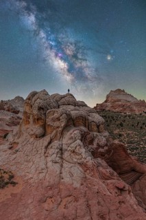 A distant unrecognizable hiker stands atop unique rock formations in Utah, USA, beneath a dazzling