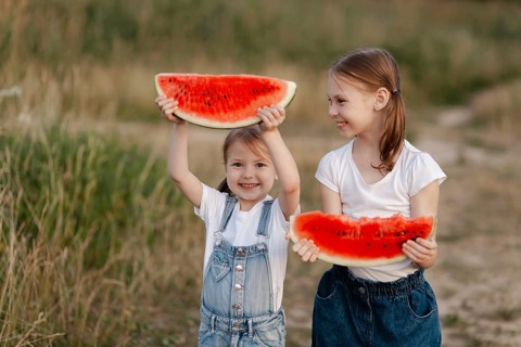 Two young children delight in the joy of summer, holding vibrant red watermelon slices in an open