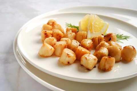 Scallops are cooked and arranged on a white plate. Fresh lemon and herbs add flavor to the dish.
