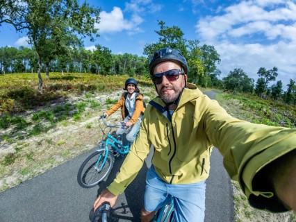 Happy couple cycling on a paved country road through green forest, taking a joyful selfie together