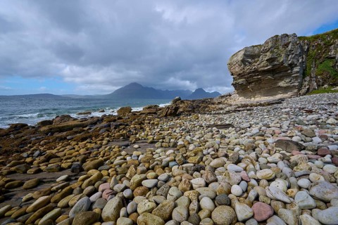 Pebble beach with rocks on the coast, under a cloudy sky with sea views in a natural, peaceful