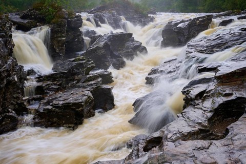 A wild, torrential waterfall flowing over dark rocks in a natural setting, River Orchy, Eas