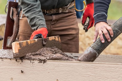 Construction Worker Leveling Wet Cement Into Wood Framing