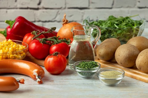 Fresh ingredients such as potatoes, tomatoes, peppers, sausage, corn, onions and arugula in a