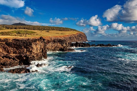 Rough sea beats against rugged cliffs under blue sky with patches of cloud, the landscape of Easter